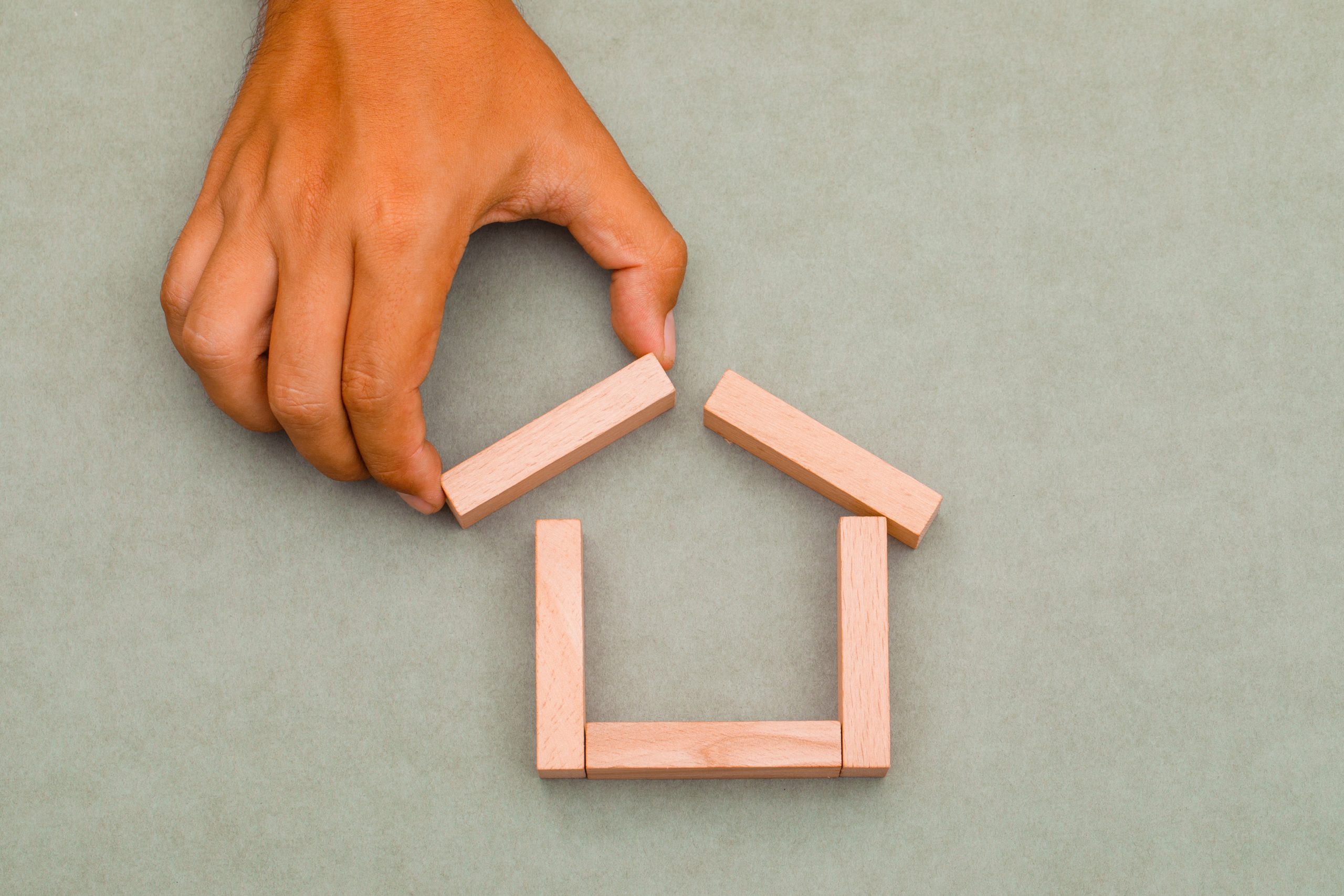 Mortgage concept on greenish grey background flat lay. man pulling out wooden block.